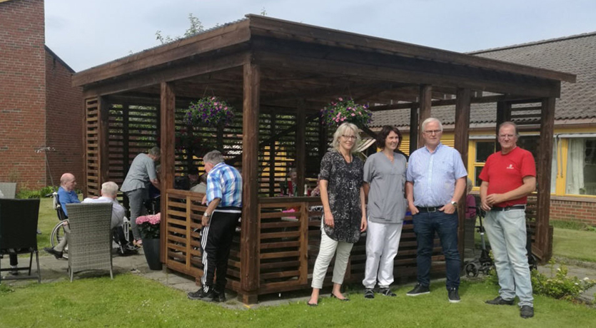 Foto av ansatte fra Surnadal sjukeheim og representanter fra Talgø foran den nye hagestuen ved Surnadal sjukeheim.