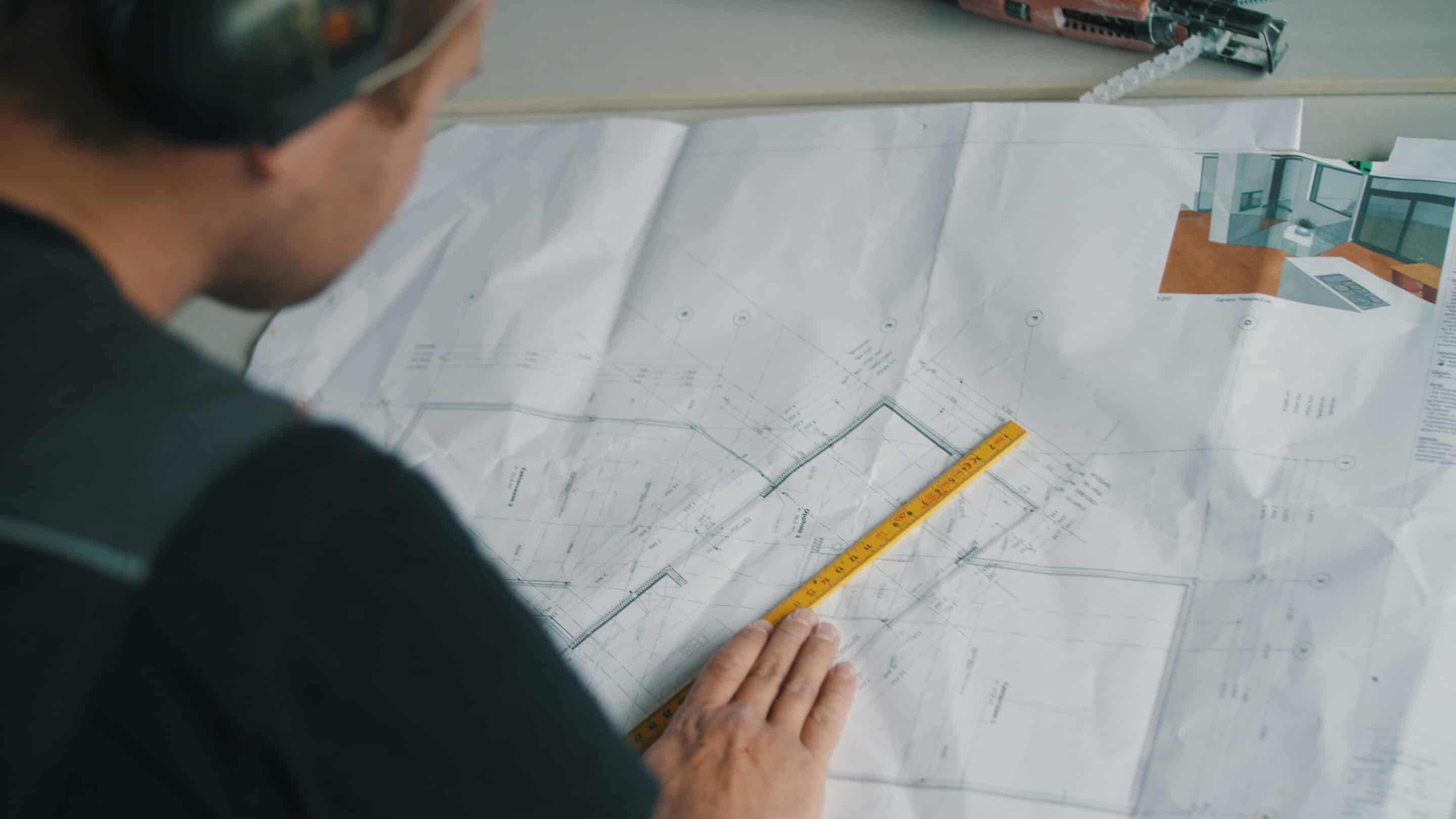 Nærbilde av snekker som studerer plantegning. Plantegning og tommestokk i fokus.