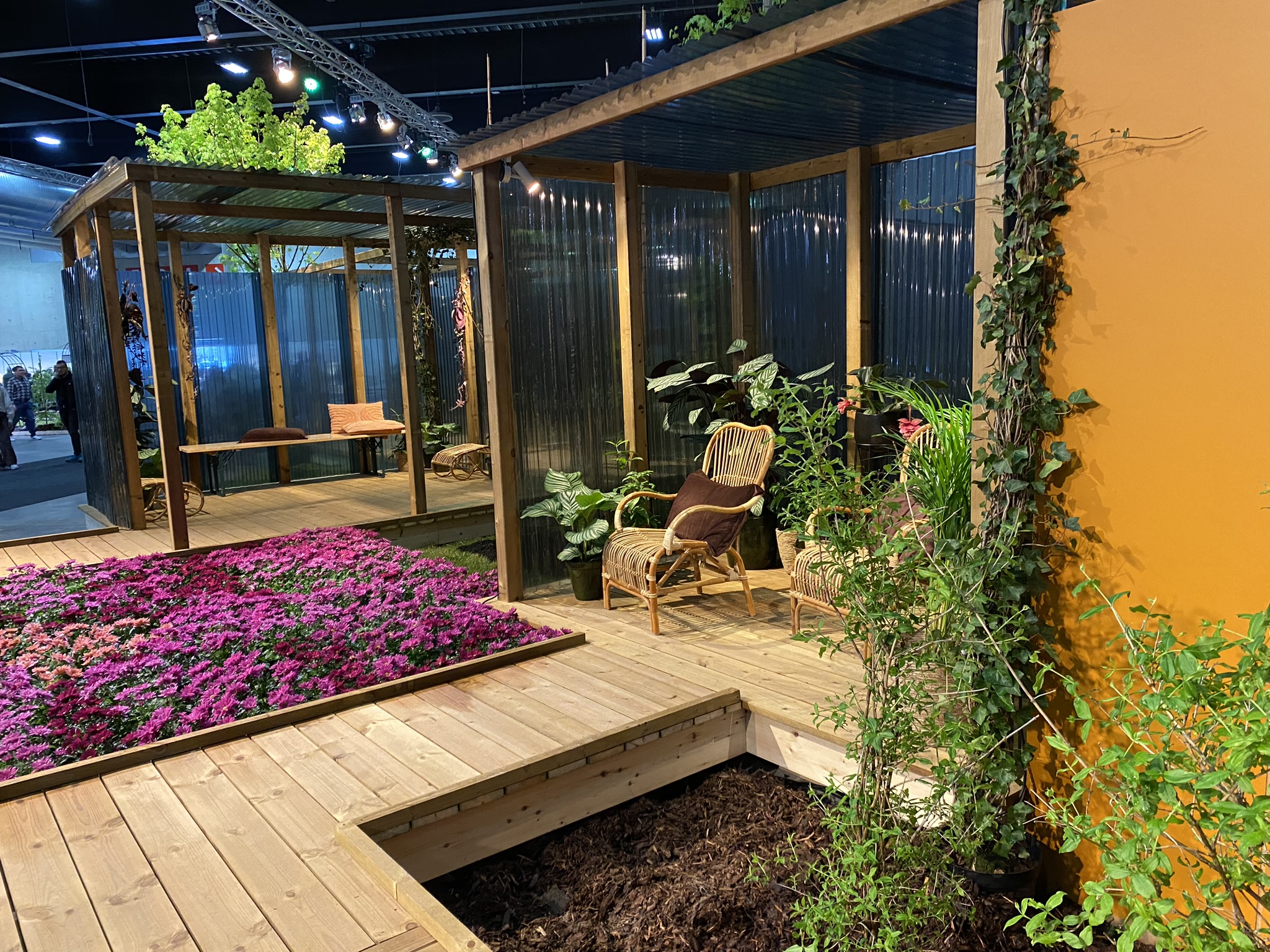 Foto av Kersti Bergesen sin Fantasihage under Hyttemessen 2024. Boardwalk i MøreRoyal. Pergola / hagestue i MøreRoyal, kombinert med materialer fra Plastmo. Bugnende planter i bed.